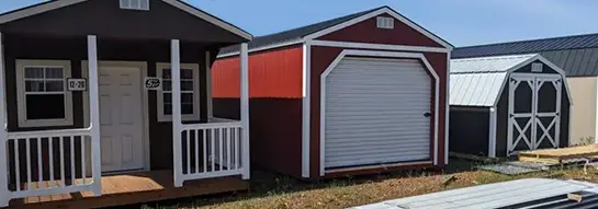 Portable buildings on display including cabin, red storage shed, and barn-style shed