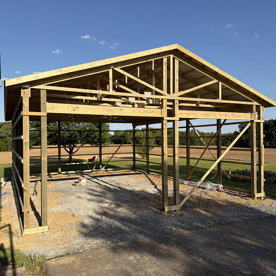 Post-frame building under construction with exposed wood posts and roof trusses